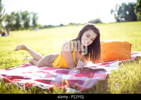 Young attractive woman reading a magazine on a meadow in a park Stock Photo