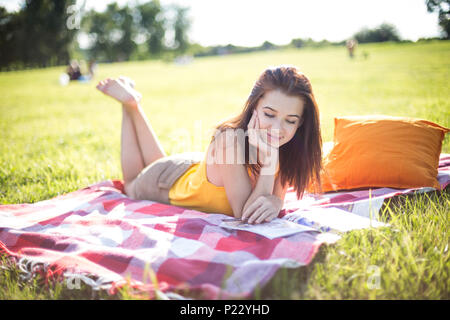 Young attractive woman reading a magazine on a meadow in a park Stock Photo