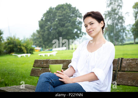 Young woman with a cup of tea sitting on a bench Stock Photo
