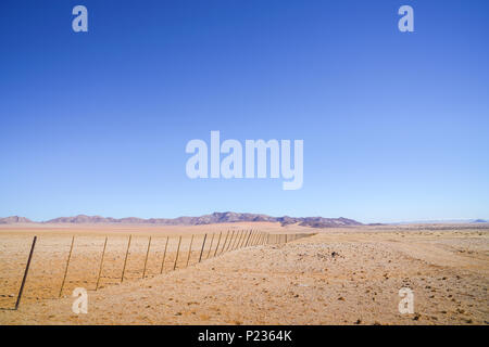 Namibia wide open desert landscape divided by long fence heading towards distant hills with red sand drifts. Stock Photo
