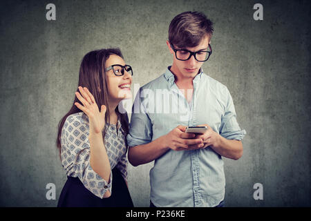 Attractive woman trying to bring attention of young handsome man ignoring her using a smartphone browsing internet. Phone addiction concept. Stock Photo