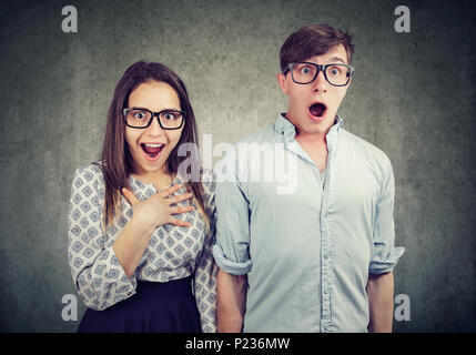 Couple of nerd man and woman in glasses standing together and looking amazed on gray background. Stock Photo