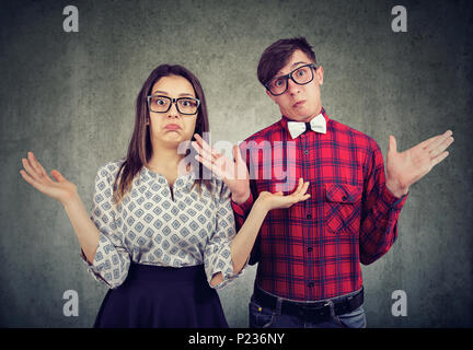 Young stylish couple in glasses looking clueless and shrugging with shoulders looking at camera. Stock Photo