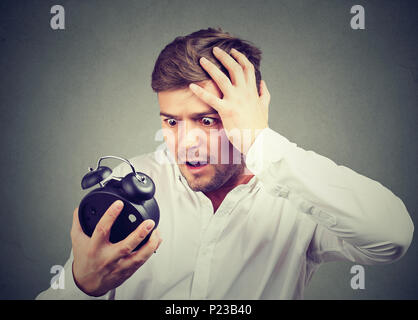 Young stressed man holding hand on head and looking at time realizing of being late. Stock Photo
