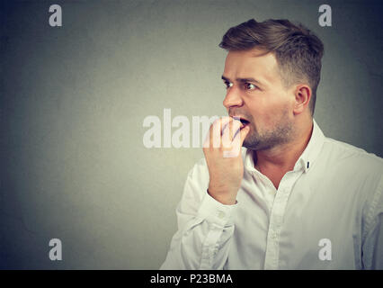 Bearded man in shirt looking away in fright and biting nails having panic attack. Stock Photo