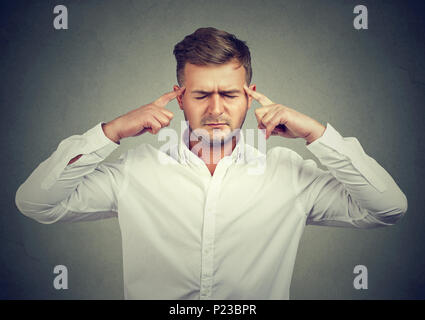 Young man rubbing temples with fingers trying to concentrate and looking for solution. Stock Photo
