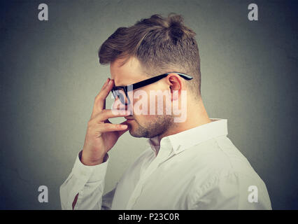Young man in elegant shirt and glasses rubbing forehead and thinking in anxiety. Stock Photo
