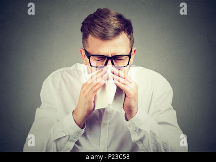 Young man in eyeglasses sneezing into handkerchief having cold and suffering from virus. Stock Photo
