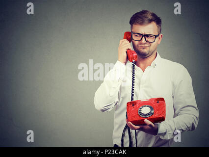 Casual man in eyeglasses talking on old-fashioned phone looking away in misunderstanding. Stock Photo