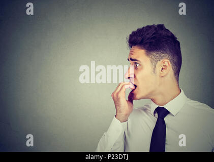 Preoccupied anxious young man biting his fingernails looking to the side Stock Photo