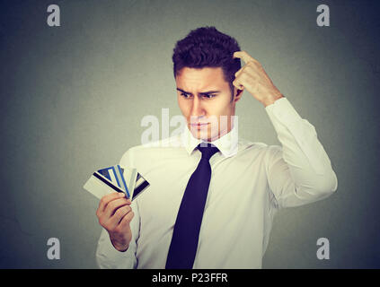 Confused man looking at many credit cards uncertain which one to choose isolated on gray background Stock Photo