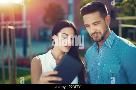 Young woman showing interesting news on tablet to man, outdoors Stock Photo