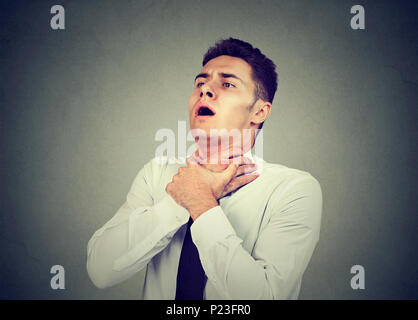 Young man having asthma attack or choking can't breath suffering from respiration problems isolated on gray background Stock Photo