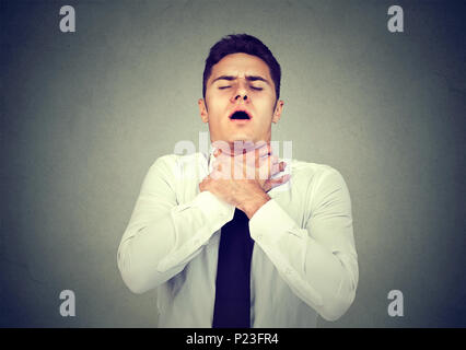 Young man having asthma attack or choking can't breath suffering from respiration problems isolated on gray background Stock Photo