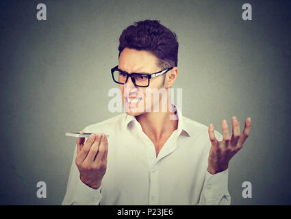 Frustrated man using a smart phone voice recognition function on line isolated on gray wall background Stock Photo