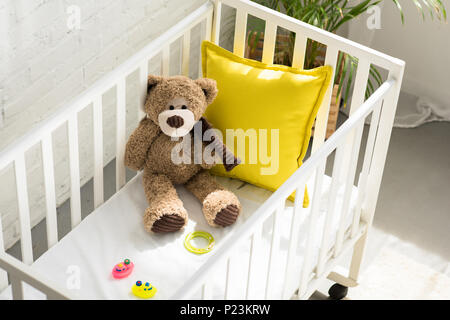 high angle view of teddy bear, other toys and yellow pillow in baby crib at home Stock Photo