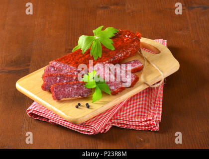 sliced air dried salami on wooden cutting board Stock Photo