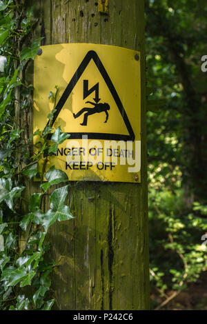 Yellow Electricity-Death sign on overhead electricity supply cable post. Death hazard, electricity warning sign, public warning sign, electrocution. Stock Photo