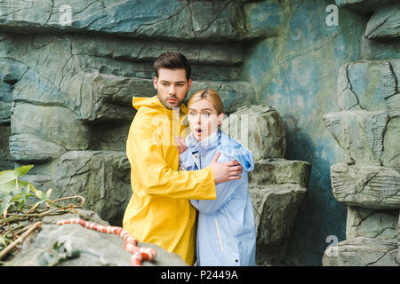 emotional young couple in raincoats terrified of snake Stock Photo