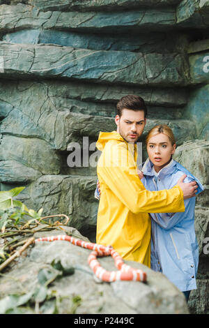frightened young couple in raincoats terrified of snake Stock Photo