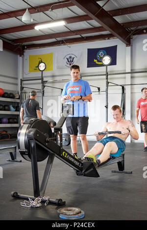 Male or man competing in a CrossFit fitness challenge competition by using a rowing machine to exhaustion inside a gym in Montgomery Alabama, USA. Stock Photo