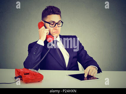 Young business man having serious telephone conversation and using tablet computer Stock Photo