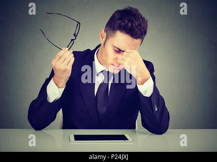 Frustrated young handsome man looking exhausted feeling tired sitting at his working place and carrying his glasses in hand Stock Photo