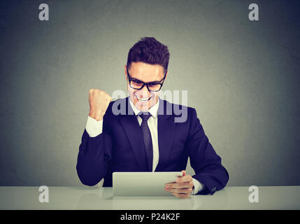 Excited business man reading good news on line on a tablet computer sitting at table in his office Stock Photo