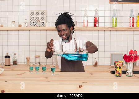 african american bartender pouring blue drink into shot glasses at bar counter Stock Photo
