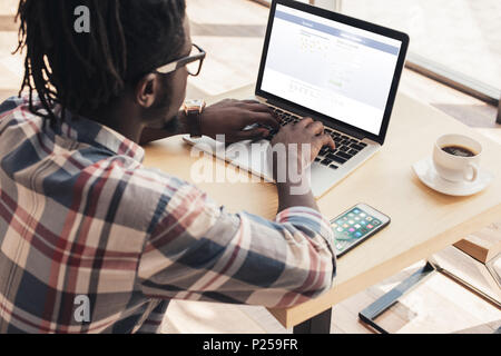 african american man using laptop with facebook website and smartphone in cafe Stock Photo