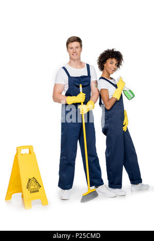 smiling multiethnic cleaners with cleaning supplies and warning sign looking at camera isolated on white Stock Photo
