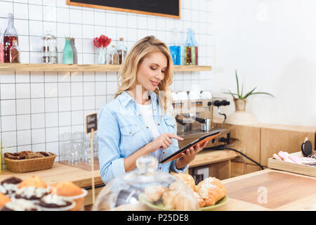 beautiful smiling young waitress using digital tablet in cafe Stock Photo