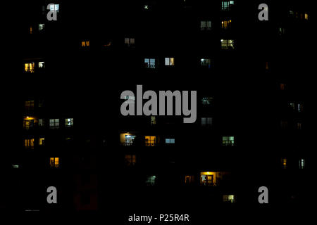 multiple windows of an apartment building at night. Some yellow, some blue, some light on, some light off. Stock Photo