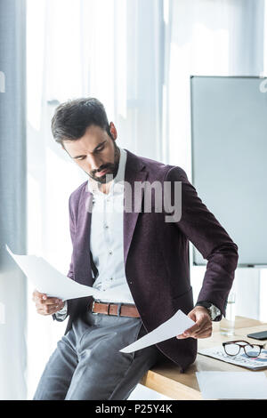 handsome young businessman doing paperwork while leaning back on desk at office Stock Photo