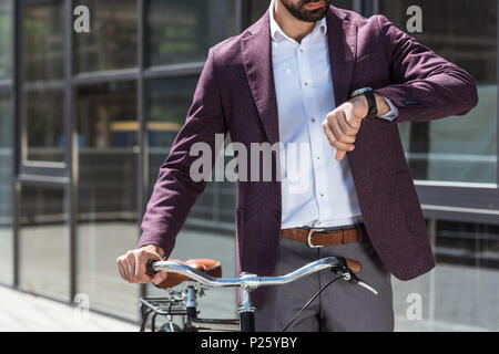 cropped shot of man in stylish suit with vintage bicycle looking at watch Stock Photo
