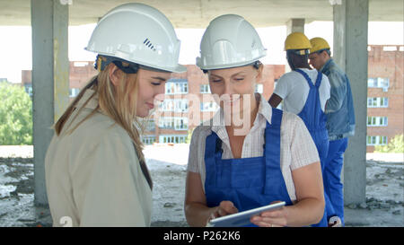 Construction worker and engineer working on building site, using digital tablet Stock Photo
