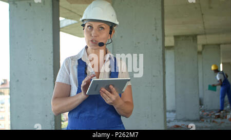 Female construction engineer reading plans using digital tablet and talk to workers through internal links Stock Photo