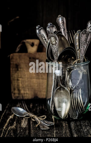 Still life with old silver cutlery in a jar and wooden boards on a wooden table Stock Photo
