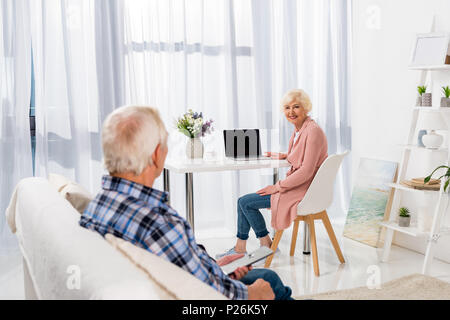 happy senior couple spending time at home while woman using laptop Stock Photo