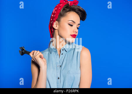 fashionable young woman in pin up style clothing with wrench isolated on blue Stock Photo