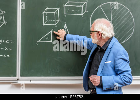 grey hair professor pointing on something with finger at blackboard Stock Photo