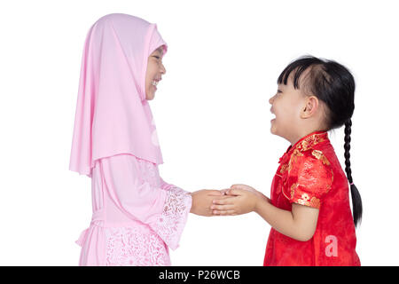 Asian Chinese little sisters wearing cheongsam and traditional Malay costume with greeting gesture in isolated white background Stock Photo