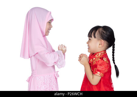 Asian Chinese little sisters wearing cheongsam and traditional Malay costume with greeting gesture in isolated white background Stock Photo