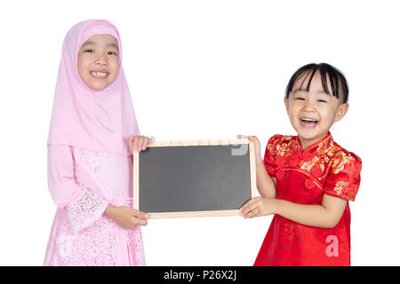 Asian Chinese little sisters wearing cheongsam and traditional Malay costume holding blackboard together in isolated white background Stock Photo