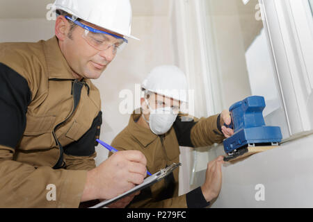 young builder in hardhat sanding wall indoors Stock Photo