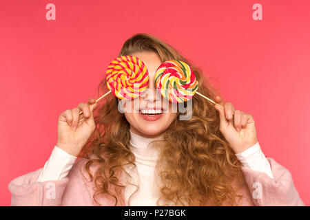 happy girl covering eyes with round lollipops isolated on red Stock Photo