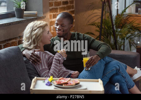 side view of smiling interracial couple with glasses of juice looking at each other at home Stock Photo