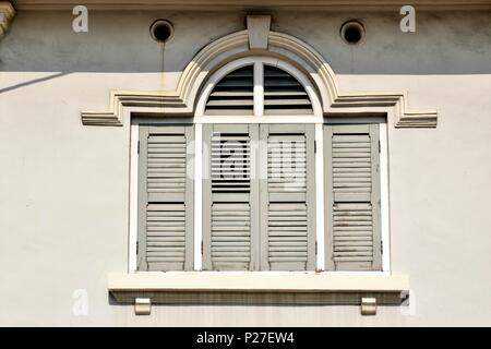 Traditional vintage Singapore shop house with antique shutters and arched window on a white wall in historic Little India Stock Photo