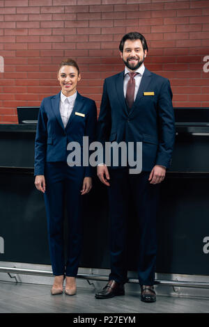 happy hotel receptionists standing together in front of counter and looking at camera Stock Photo