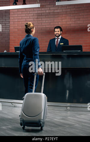 businesswoman with luggage going at hotel reception counter Stock Photo